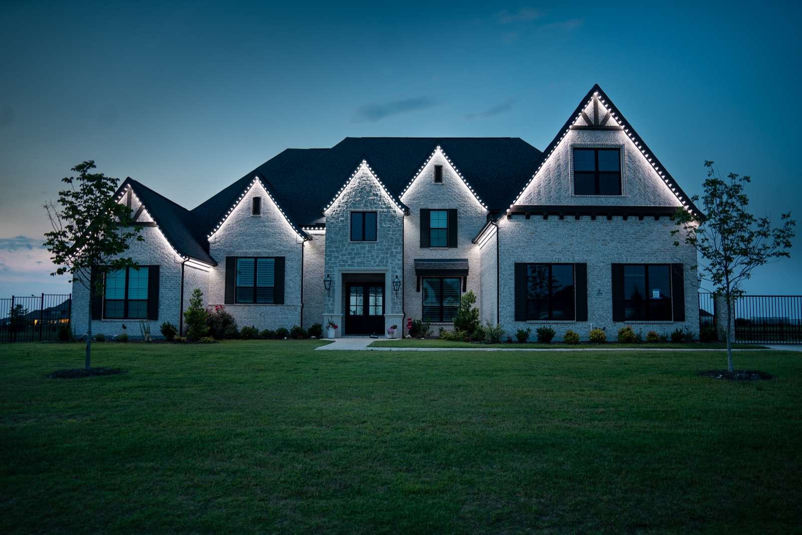 A Central Texas home at dusk, permanent lighting tracing the roofline
